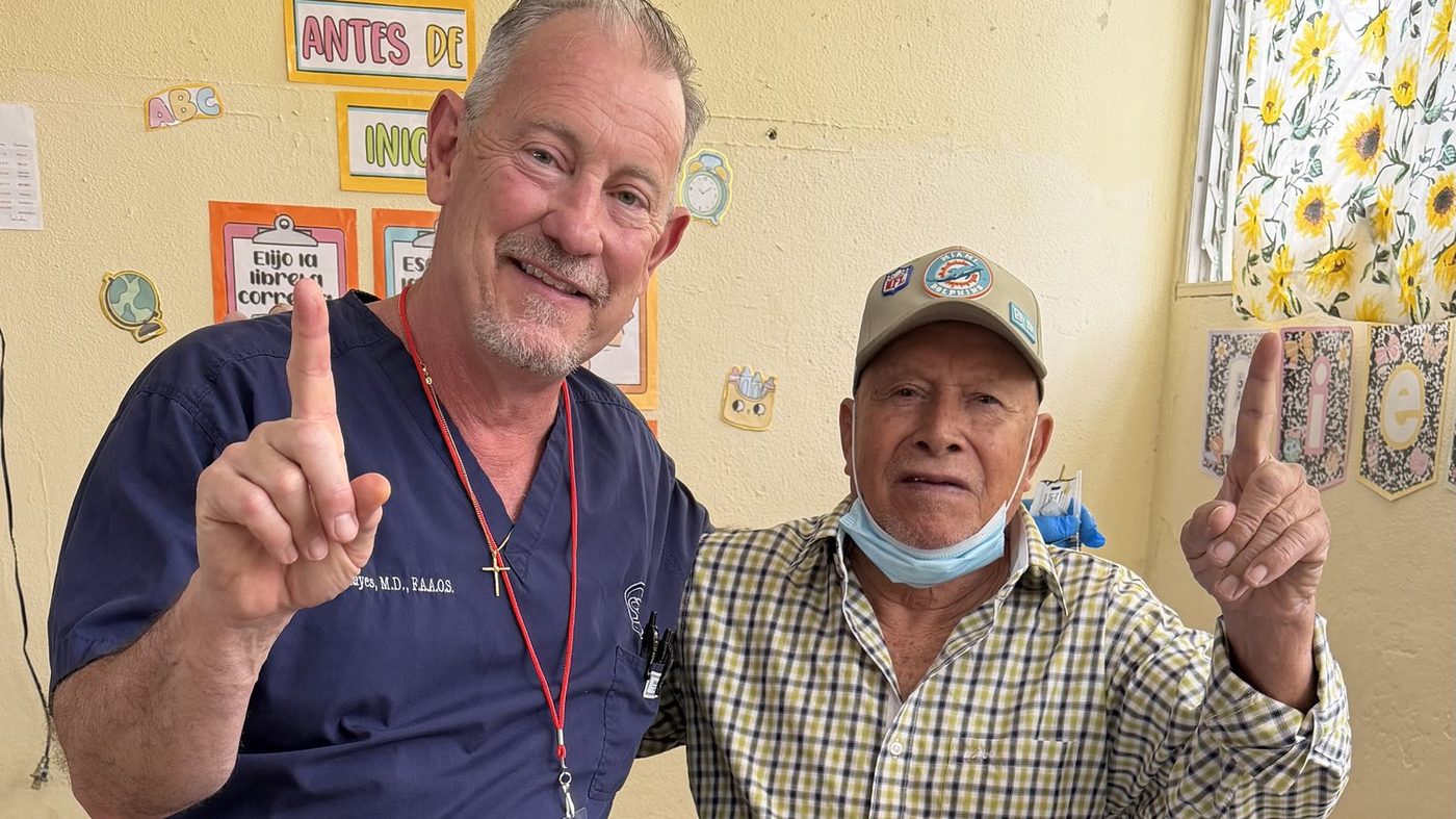 Dr. Bill Hayes in scrubs with a smiling patient on a medical mission trip